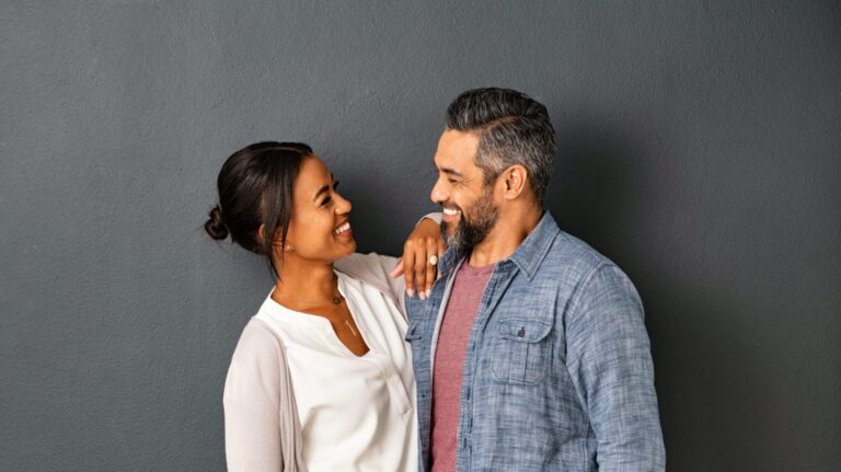 Mid adult multiethnic couple in love standing against grey wall.