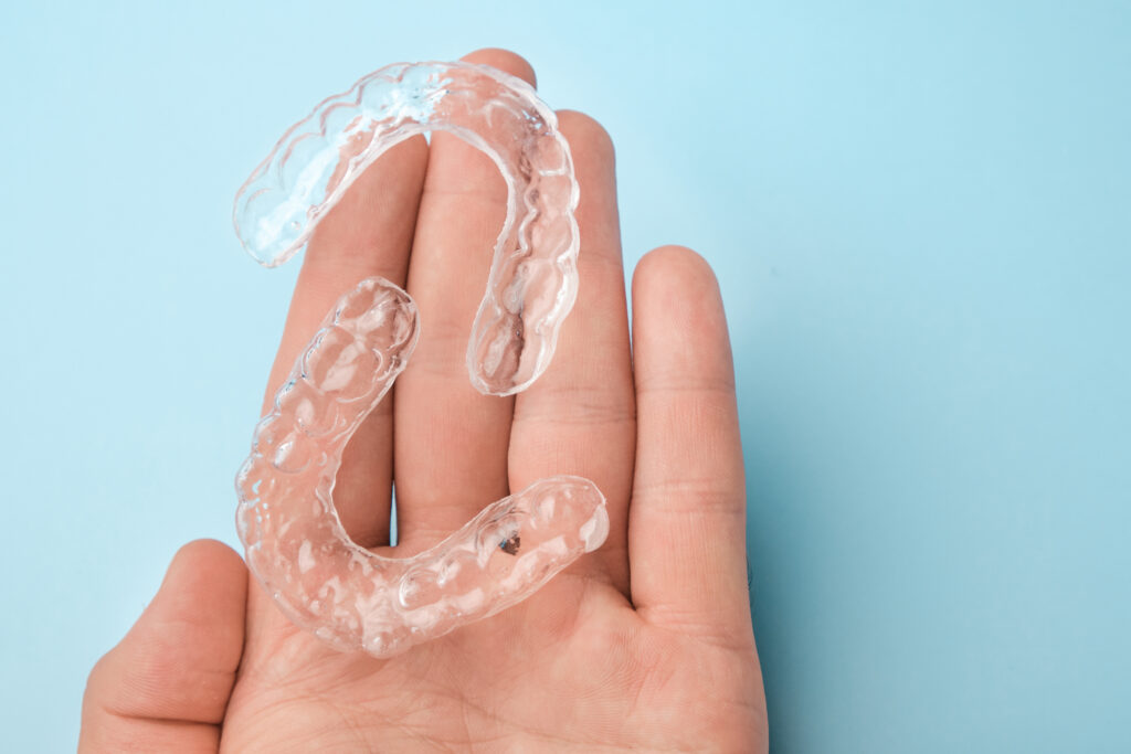 Close up mans hand holding invisible aligners for whitening and straightening of teeth on the blue background.