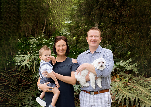 Family with a dog smiling in front of greenery